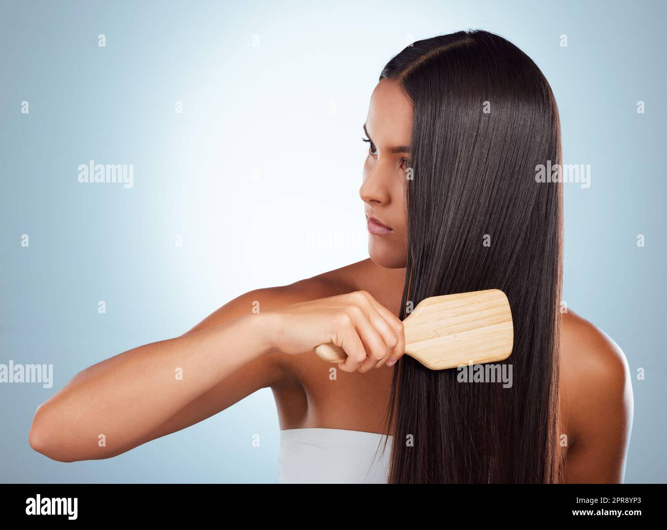 Eine schöne junge Mischrassenfrau, die ihr gesundes, kräftiges Haar vor einem grauen Studiohintergrund putzt. Hispanische Frau, die ihr Haar stöhnt Stockfoto