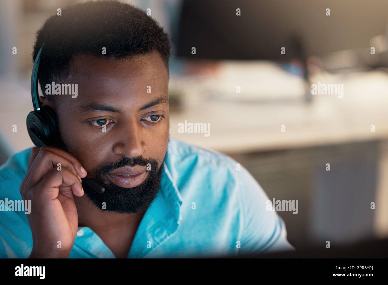 Ein junger afroamerikanischer Callcenter-Telemarketing-Agent, der während der Arbeit in einem Büro mit einem Headset spricht. Fokussierter Geschäftsberater, der einen Helpdesk für den Kundendienst betreibt Stockfoto
