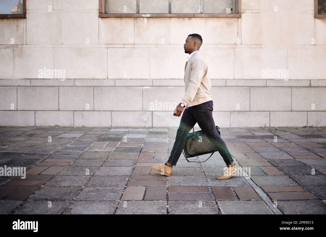 Ein afroamerikanischer Geschäftsmann, der mit seinem Gepäck durch die Stadt läuft und gleichzeitig in der Stadt stilvoll aussieht Stockfoto