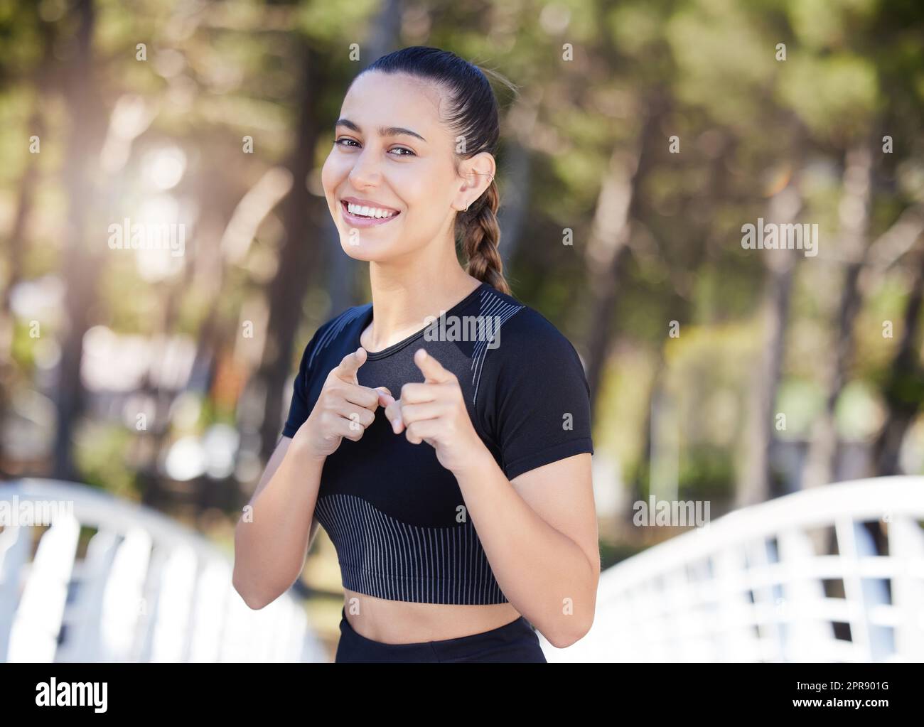 Fitnessfrau lächelt und zeigt mit dem Zeigefinger auf die Kamera, während sie im Park läuft. Fröhliche Sportlerin motiviert dich, zu trainieren und für deine Gesundheit zu sorgen Stockfoto