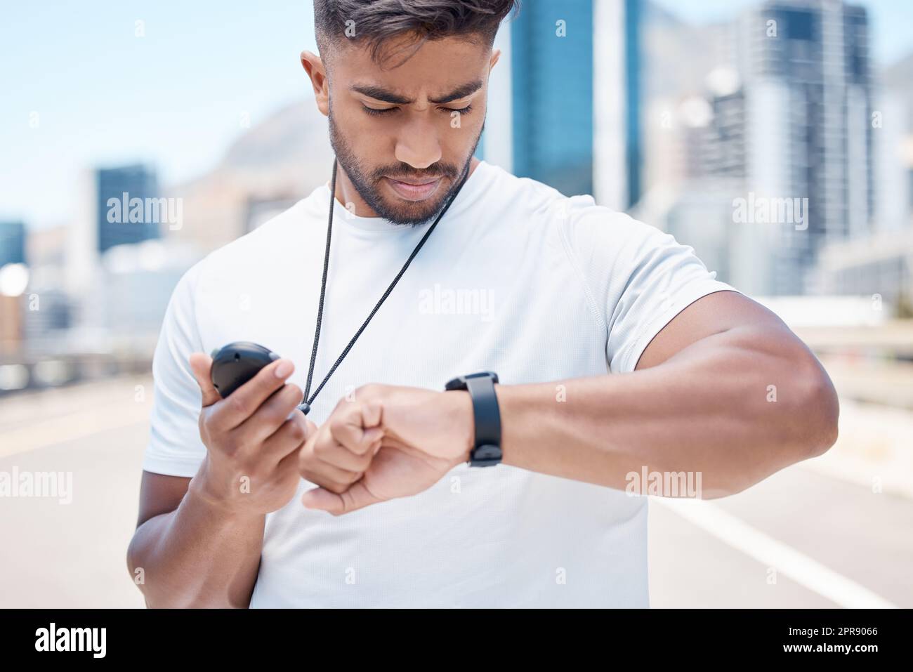 Junger männlicher Sportler mit gemischten Rassen, der den digitalen Chronometer und die Smartwatch überprüft, um die Zeit während eines Workouts aufzuzeichnen. Ein Sportler überwacht seine Leistung oder seinen Fortschritt während eines Laufs in der Stadt Stockfoto