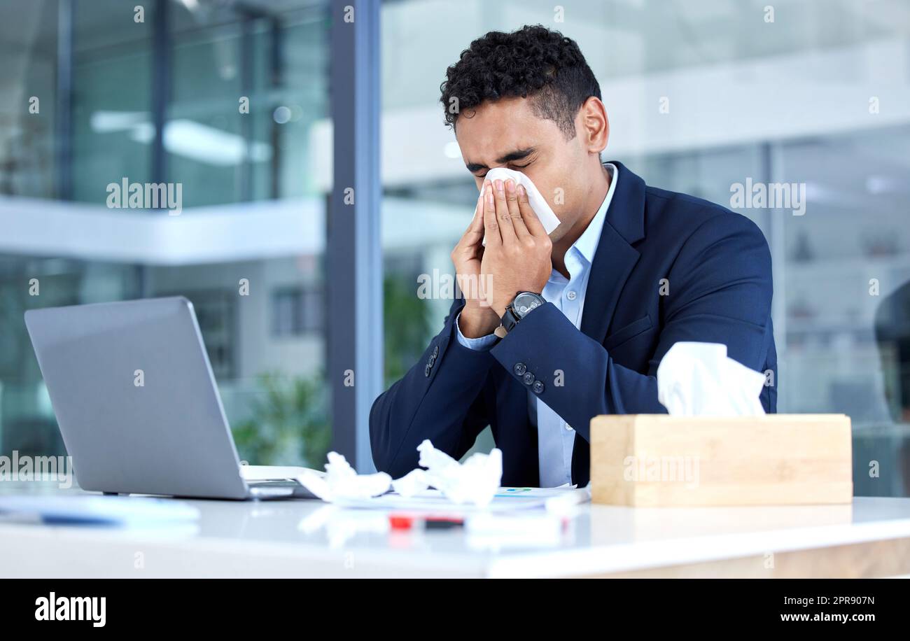 Ein kranker Geschäftsmann gemischter Rassen bläst laufende Nase mit Taschentuch, während er in einem Büro arbeitet. Hispanischer Kerl fühlt sich unwohl mit Grippe, Erkältung und covid-Symptomen. Leiden mit Stauung, Sinus und jahreszeitlicher Frühjahrsallergie Stockfoto