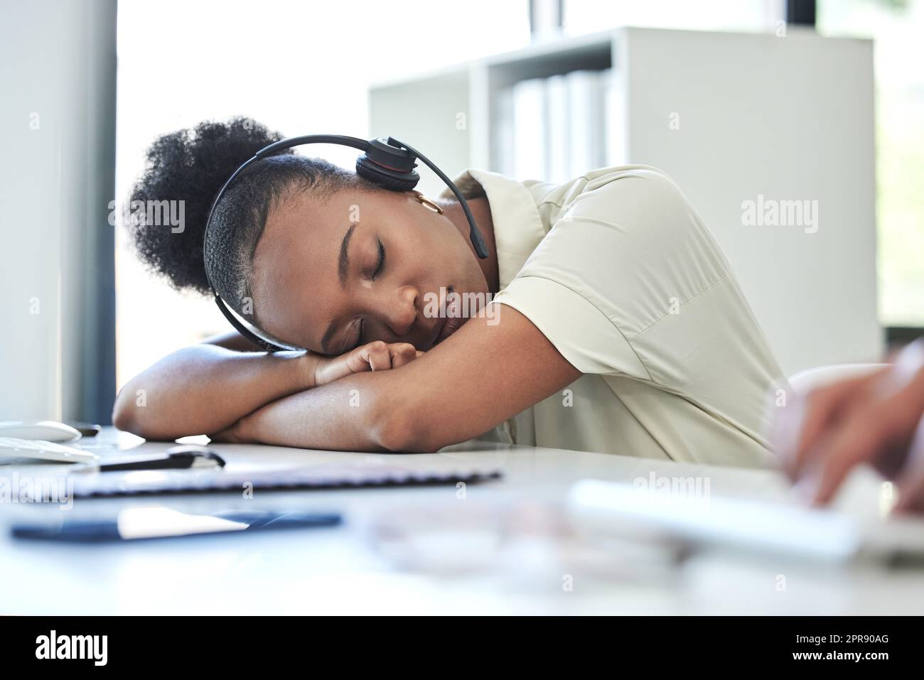 Ein fünfminütiges Nickerchen wirkt Wunder. Eine attraktive junge Callcenter-Agentin schläft auf ihrem Schreibtisch im Büro. Stockfoto