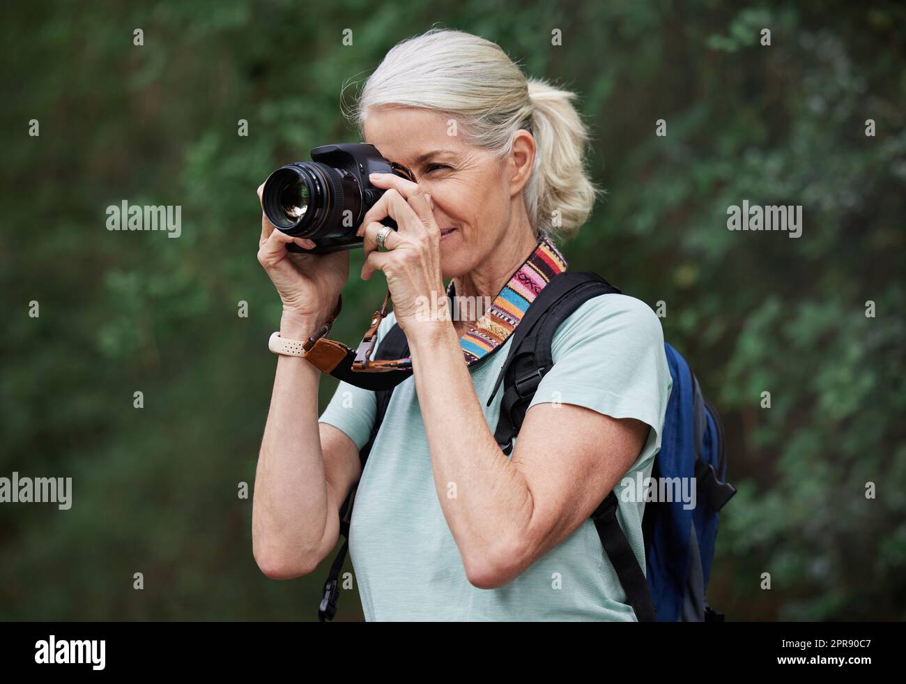 Eine reife weiße Frau, die beim Wandern Fotos mit der Kamera macht. Seniorin, die mit ihrer drahtlosen Digitalkamera Fotos in der Natur bei einer Wanderung im Freien macht Stockfoto