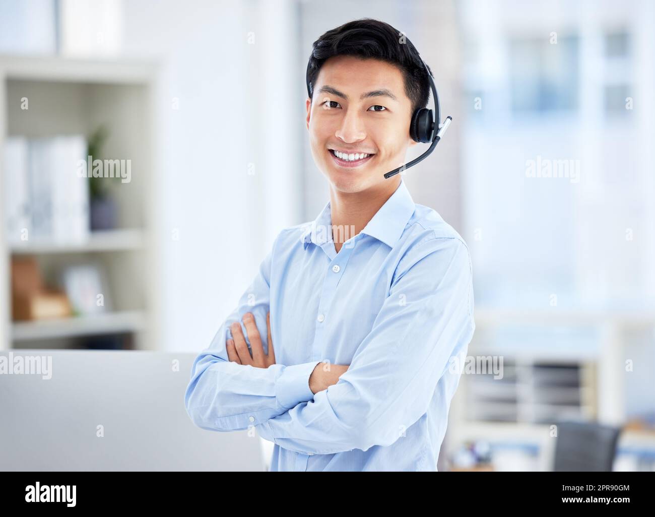 Porträt eines asiatischen Callcenter-Agenten, der im Büro mit gekreuzten Armen ein Headset trägt. Selbstbewusster und lächelnder Geschäftsmann, der einen Helpdesk für den Vertrieb und Service betreibt Stockfoto