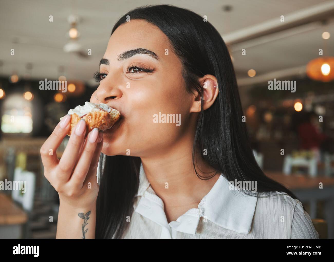 Die perfekte Zeit zum Genießen. Eine schöne junge Frau, die in einem Café zu einem leckeren Leckerbissen beißt. Stockfoto