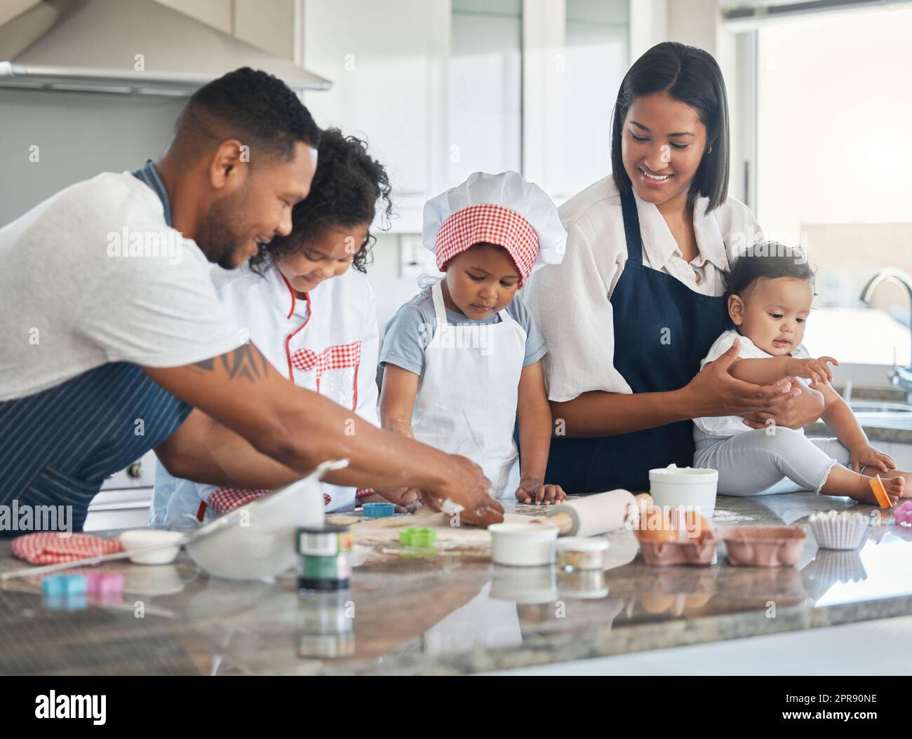 Backen ist mies, chaotisch und lecker, weshalb Kinder es lieben. Ein Paar, das mit ihren drei Kindern zu Hause bäckt. Stockfoto