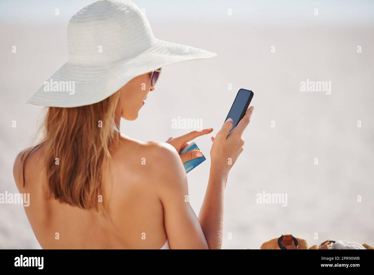 Frau mit Kreditkarte im Urlaub. Eine junge Frau mit ihrem Telefon und Kreditkarte am Strand. Stockfoto