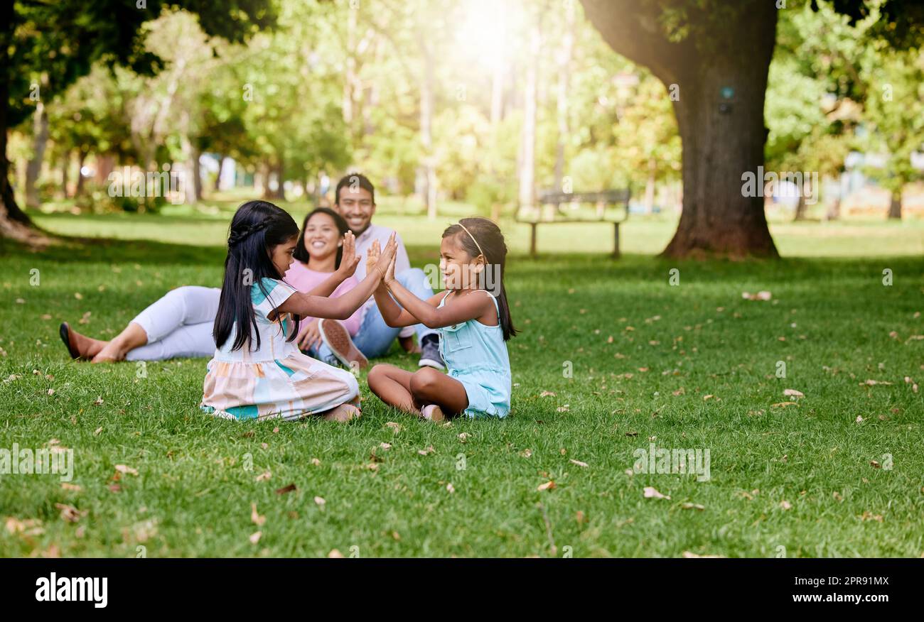 Ein glückliches asiatisches Paar, das draußen auf dem Rasen liegt, liebevolle Eltern genießen eine schöne Zeit mit ihren kleinen Töchtern, die ein Spiel spielen. Ein Paar, das sich während der Familienzeit im Park mit seiner adoptierten Pflegeschwester verbindet Stockfoto