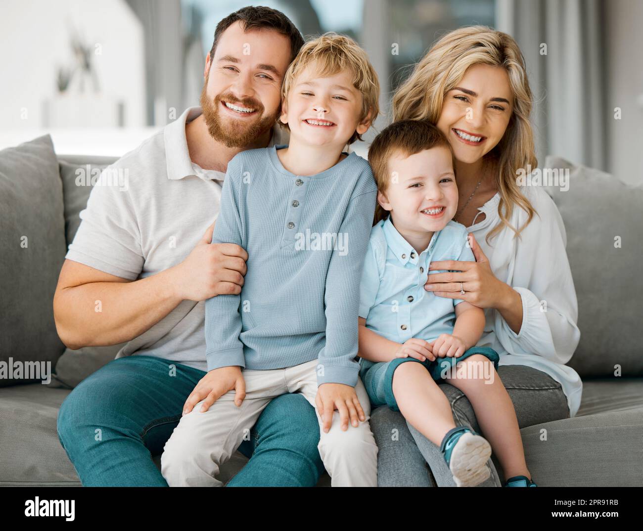 Porträt einer glücklichen weißhäutigen Familie, die entspannt auf dem Sofa zusammensitzt. Süße kleine Jungs, die mit ihren liebenden Eltern auf dem Sofa chillen, während sie lächeln und positiv aussehen Stockfoto