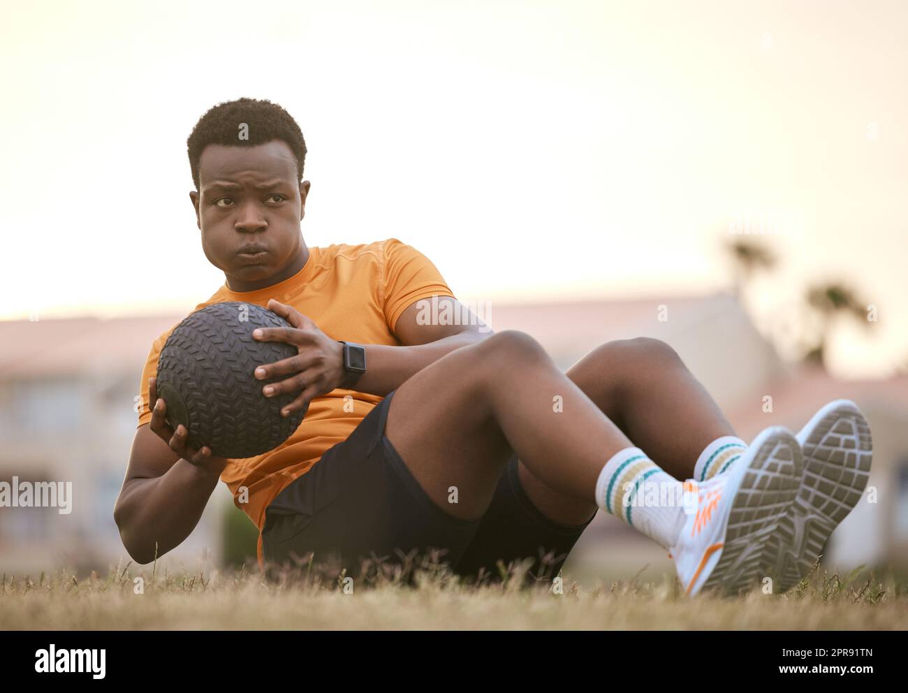 Ein sportlicher Mann, der Sport treibt, an seiner Fitness arbeitet. Ein afroamerikanischer Sportler, der einen Medizinball benutzt, einen aktiven, gesunden Lebensstil lebt, auf dem Gras sitzt und Sit-ups macht Stockfoto