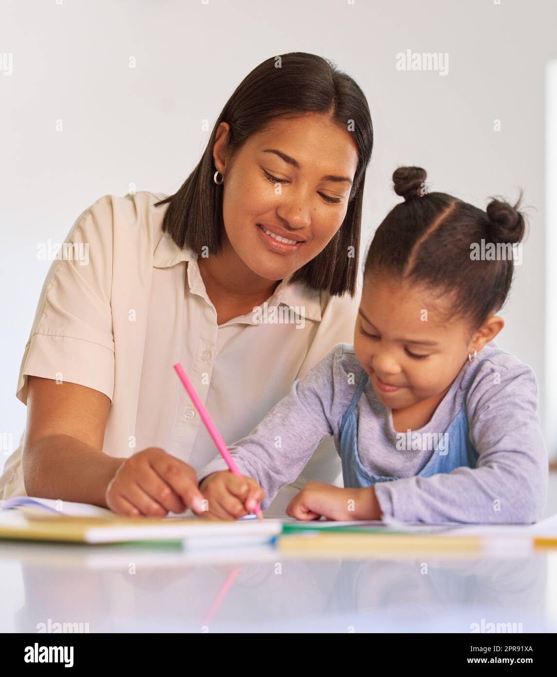Gemischte Rassenmädchen lernen und lernen mit mom im Hausunterricht. Eine Frau, die ihrer Tochter bei Hausaufgaben und Aufgaben zu Hause hilft. Fröhliche Eltern bringen dem Kind bei, zu Hause zu malen und zu schreiben, während es abgeriegelt ist Stockfoto