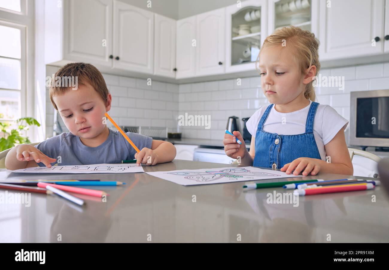 Junge weiße Geschwister, die mit Buntstiften zeichnen, während sie zu Hause an der Küchentheke sitzen. Bruder und Schwester sind kreativ in Bildern zu Hause Stockfoto