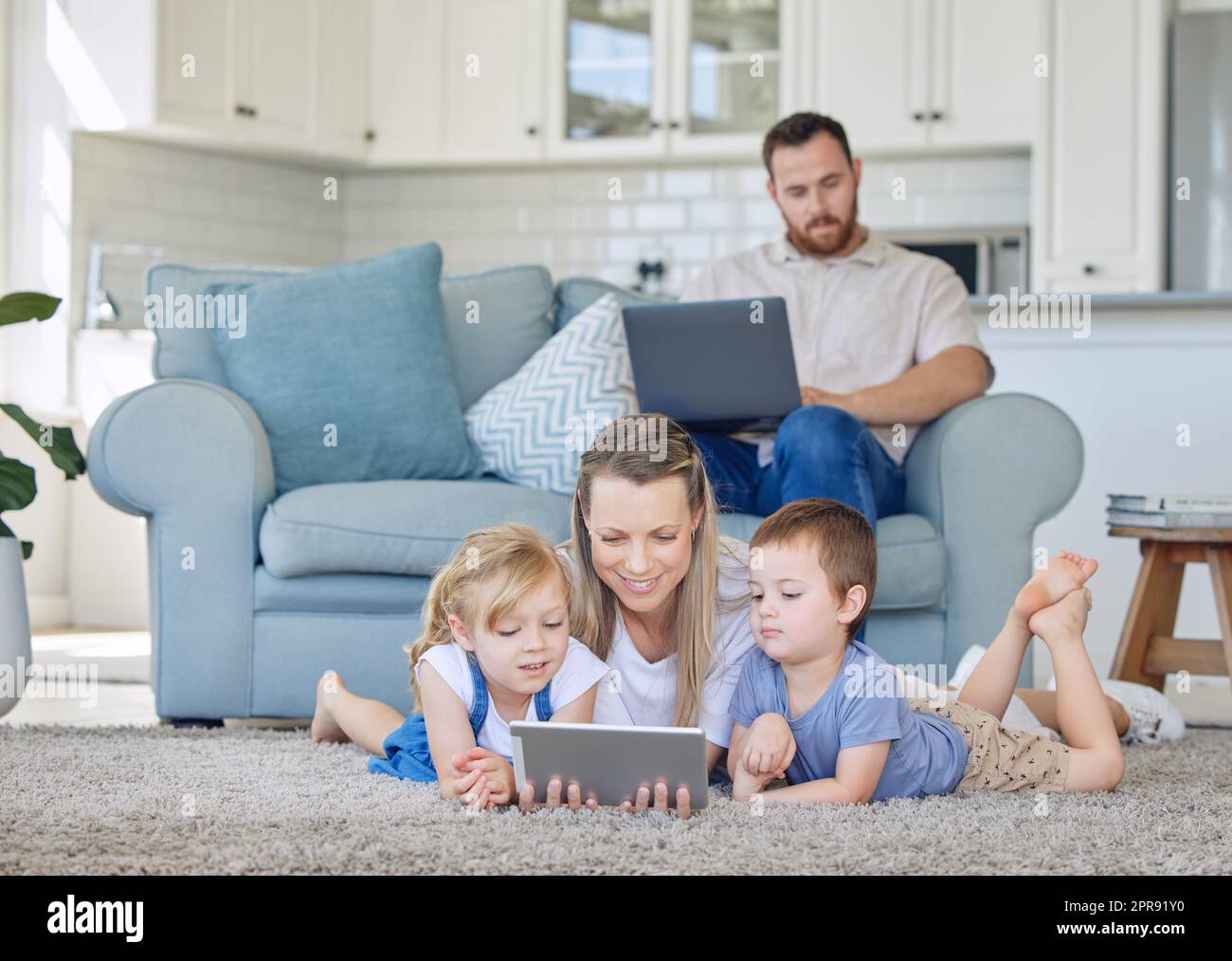 Mutter und zwei Kinder schauen sich etwas auf einem digitalen Tablet an. Kleine Mädchen und kleine Jungen sehen sich mit dem Tablet-PC Comicvideos an oder telefonieren mit ihnen. Dad arbeitet von zu Hause aus Stockfoto