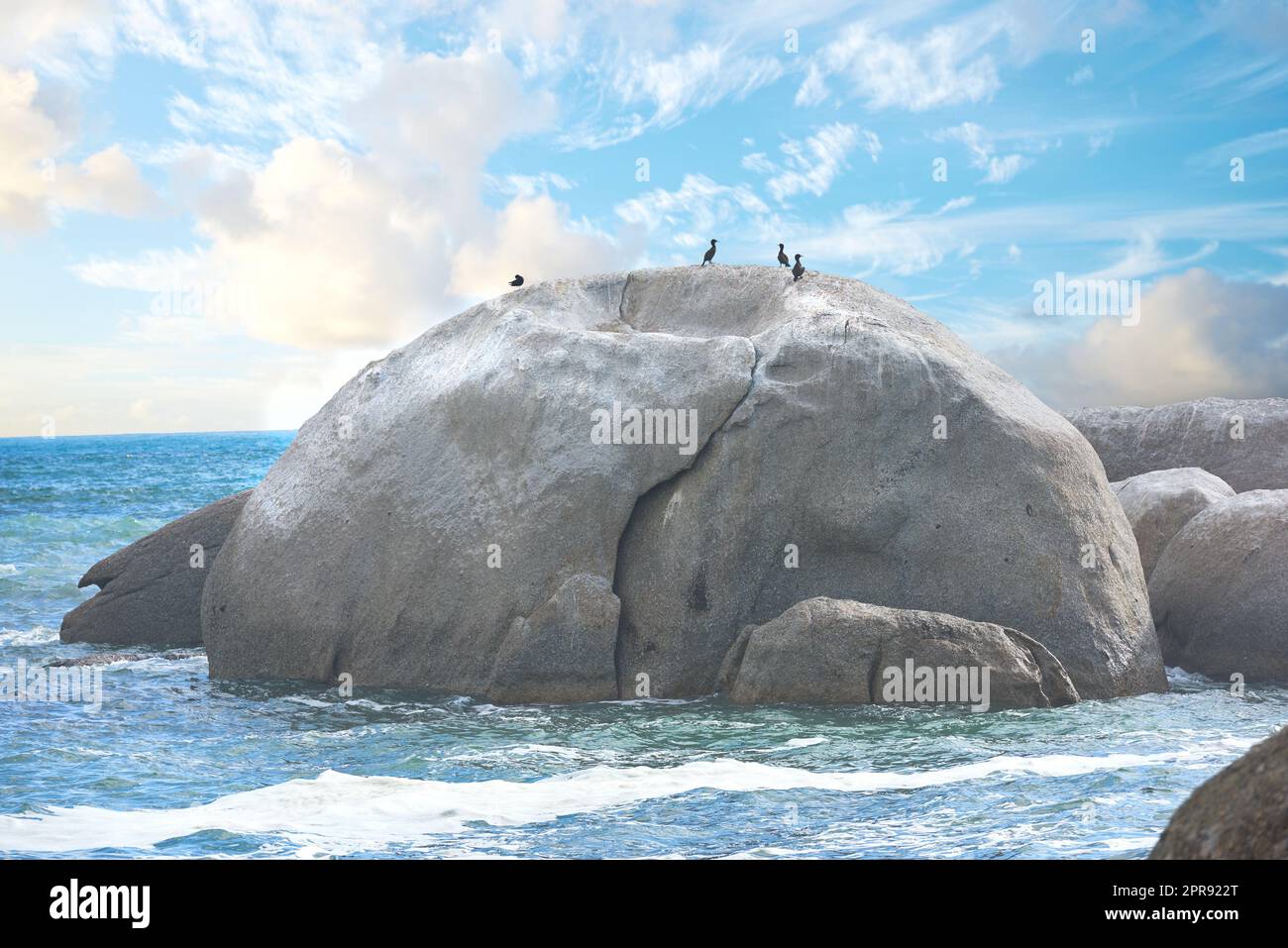 Malerischer Blick auf einen Strand mit Felsen oder Felsen und Meerwasser. Die Landschaft einer felsigen Küste im Frühling. Ein großer Felsen in der Mitte des Ozeans mit Vögeln und blauem Himmel im Sommer. Stockfoto