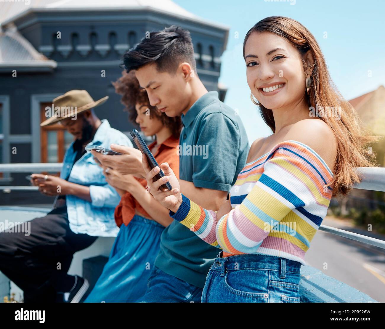 Porträt einer wunderschönen jungen lächelnden asiatischen Frau, die mit Freunden draußen steht und ihr Handy benutzt, um im Internet zu surfen. Gruppe verschiedener Millennials, die ihre Telefone nutzen, um sich mit Social medi zu verbinden Stockfoto