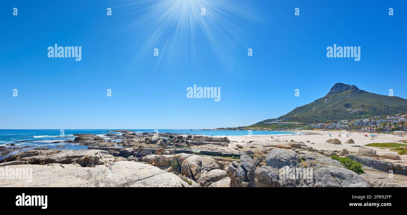 Panoramablick auf einen felsigen Strand in der Nähe des Ozeans und der Berge an einem sonnigen Tag in Südafrika. Landschaftstapete an der Küste mit Löwenkopf vor blauem Horizont mit Sonnenschein und Kopierraum im Sommer Stockfoto