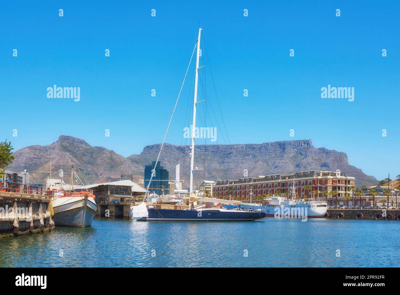 Segelboote legten an einem Hafen an, mit Tafelberg im Hintergrund vor blauem Himmel mit Kopierraum. Landschaftlich reizvolle Hafenlandschaft an einem Yachthafen. Seeschiffe für Reise und Tourismus Stockfoto