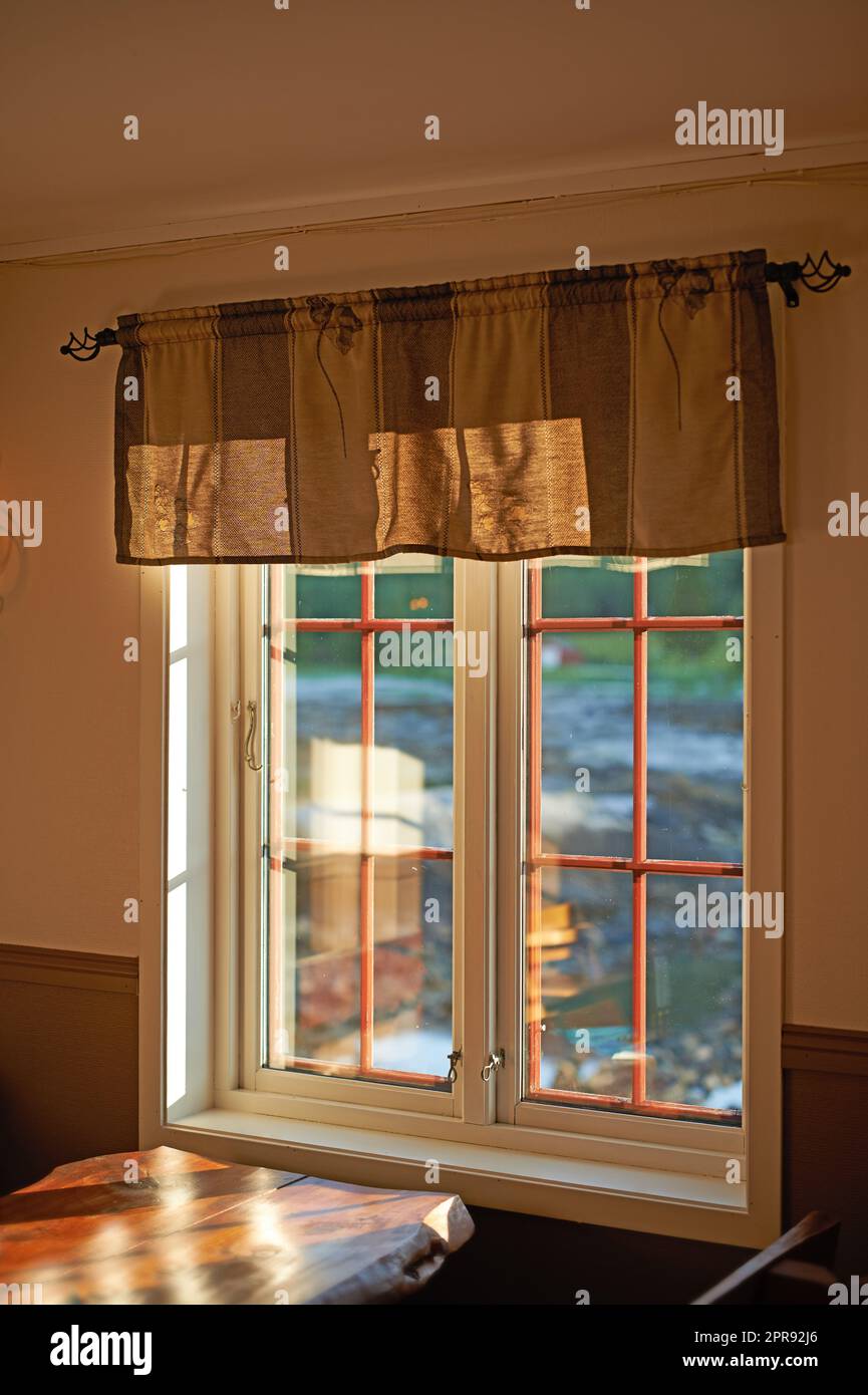 Großes Küchenfenster mit Sonnenlicht auf einem Holztisch. Rustikales Haus mit einem Blick nach draußen, der das Zimmer im Sommer beleuchtet. Gemütliche Ecke in einem Haus, wo man sitzen und Familienurlaub und Mahlzeiten genießen kann Stockfoto