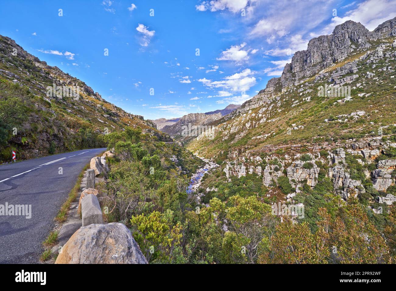 Leere Straße in den Bergen mit einem wolkigen blauen Himmel. Landschaft einer Landstraße für die Fahrt auf einem Bergpass entlang einer malerischen Naturstraße mit Grün und Blick auf die sanften Hügel Stockfoto