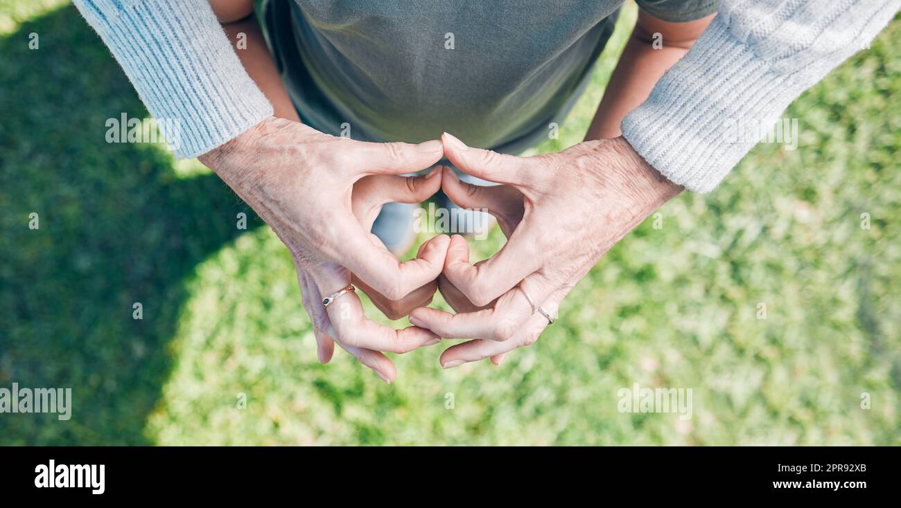 Mit Liebe pflegen. Ein unerkennbarer kleiner Junge und seine Großmutter halten ihre Hände in Herzform außen zusammen. Stockfoto