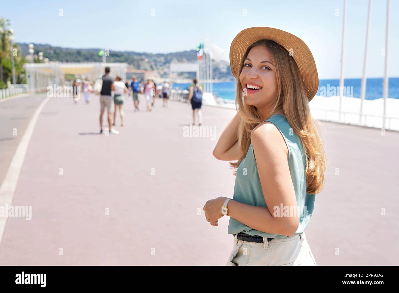 Porträt einer attraktiven Modefrau dreht sich um und lächelt der Kamera zu, die entlang der Promenade des Anglais, Nizza, Frankreich, läuft Stockfoto