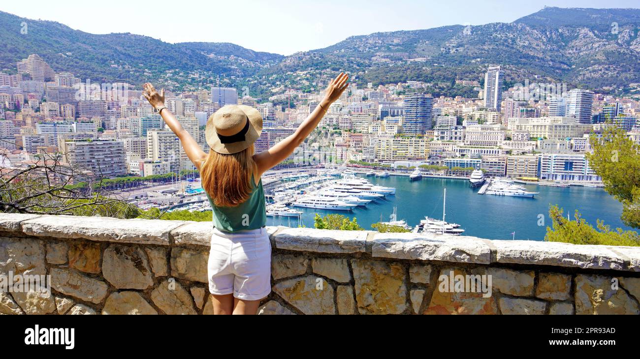 Wunderschöne Panorama-Banneransicht einer jungen Frau, die die Waffen auf dem Stadtbild von Monte-Carlo und dem Yachthafen von Monaco hochhebt Stockfoto