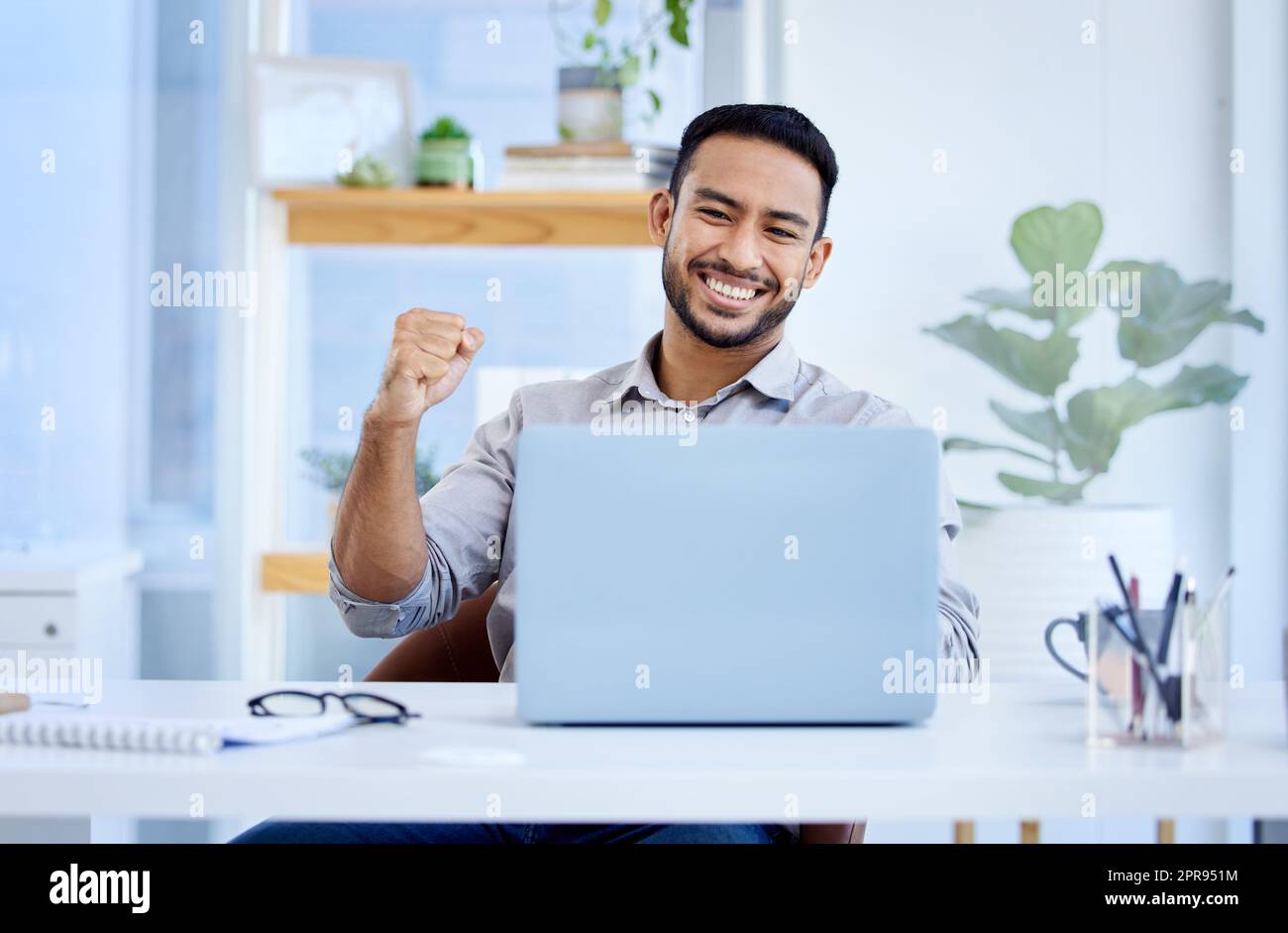 Ein junger Geschäftsmann jubelt an, während er in einem Büro an einem Laptop arbeitet. Stockfoto