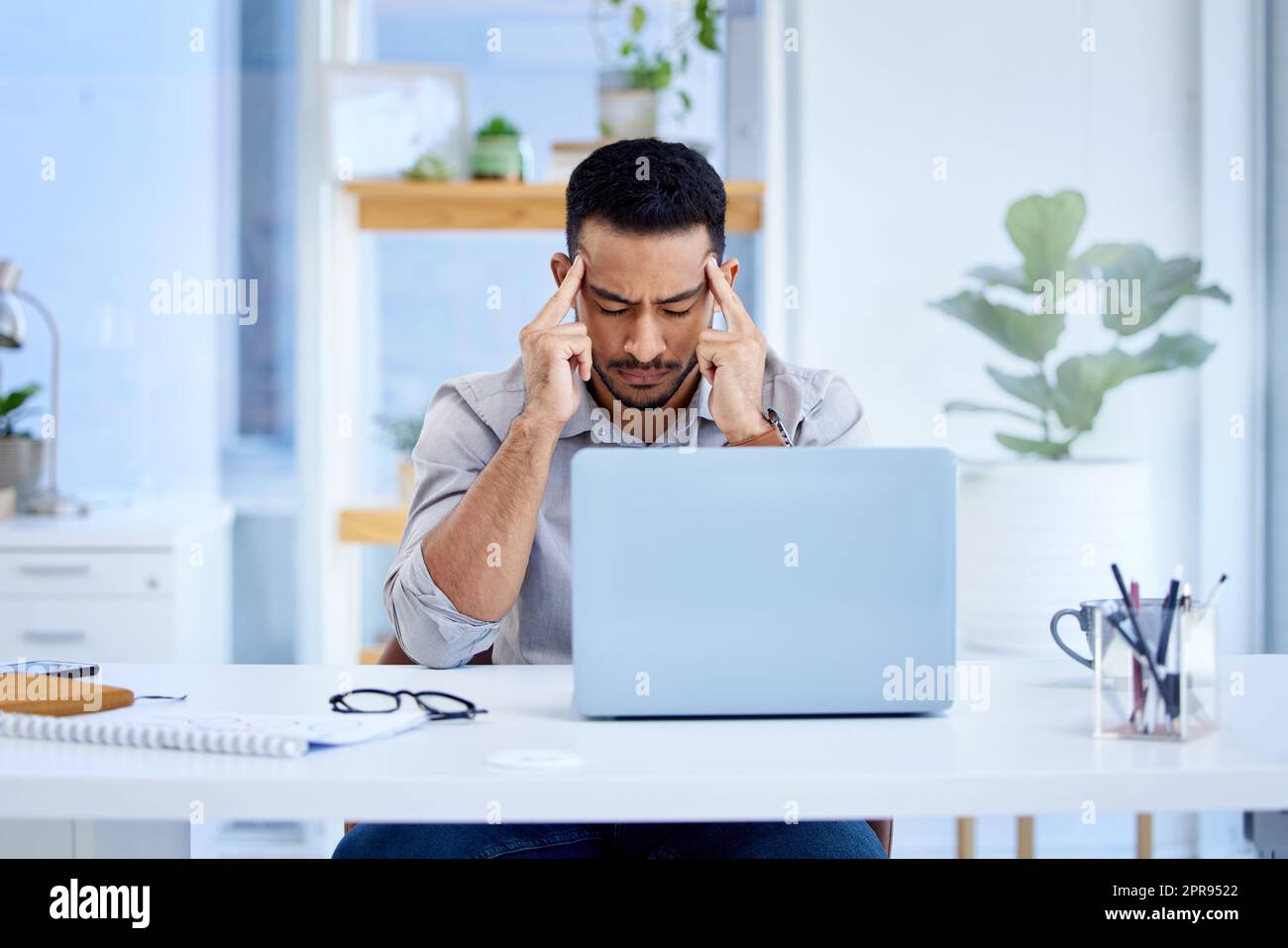Belastet durch viele sich abzeichnende Fristen. Ein junger Geschäftsmann, der gestresst auf einem Laptop in einem Büro arbeitet. Stockfoto