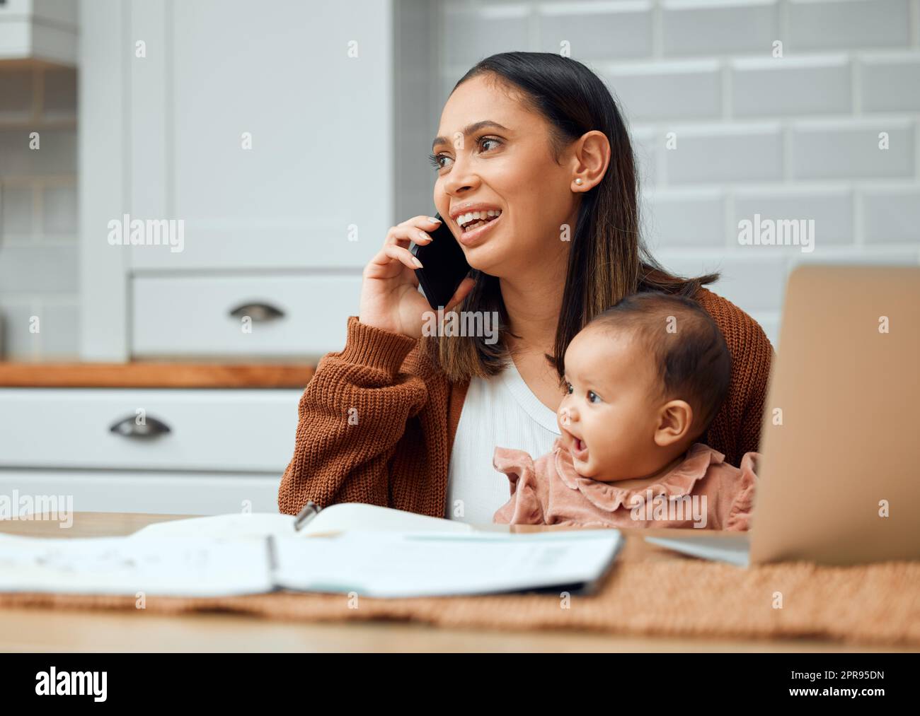 Sie ist ein Pauschalangebot. Eine attraktive junge Frau, die zu Hause arbeitet und ihr neugeborenes Baby auf ihrem Laptop sitzt. Stockfoto