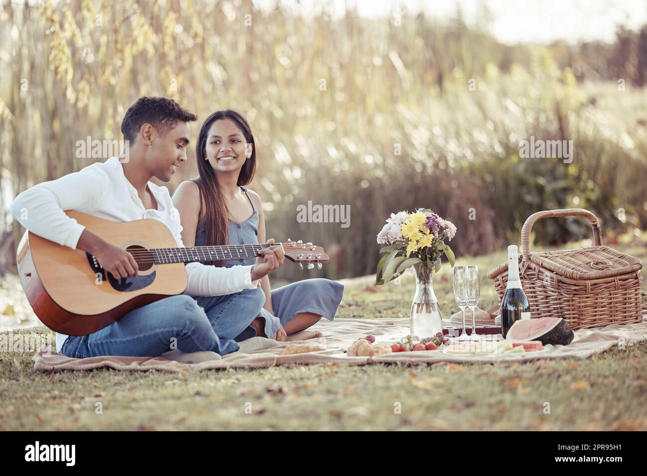 Meine Liebe durch Musik teilen. In voller Länge eine junge Frau, die mit ihrem Freund sitzt, während er während ihres Picknickdatums Gitarre spielt. Stockfoto