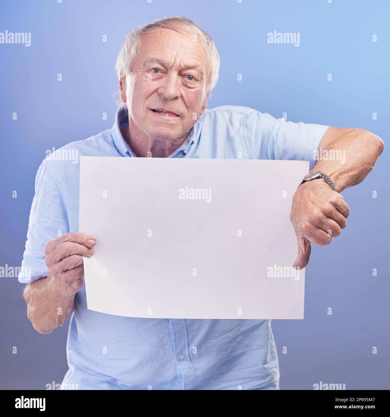 Der Service hier ist schlecht. Studioaufnahme eines älteren Mannes, der ein leeres Schild hält und den Daumen vor blauem Hintergrund zeigt. Stockfoto