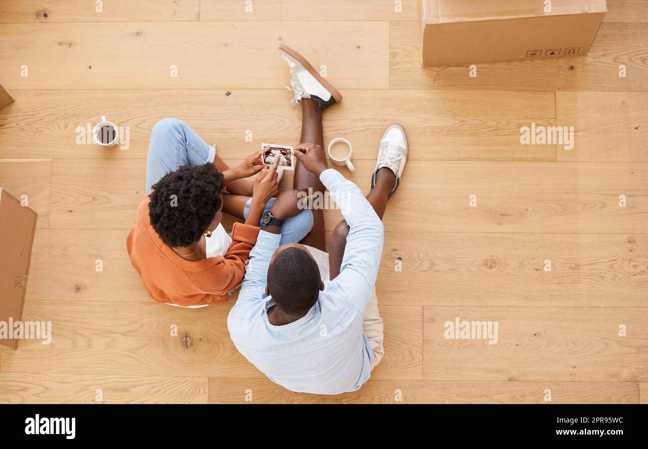 Ein neues Kapitel unseres Lebens: Ein junges Paar, das zu Hause auf dem Boden sitzt und ein Ultraschallbild anschaut. Stockfoto