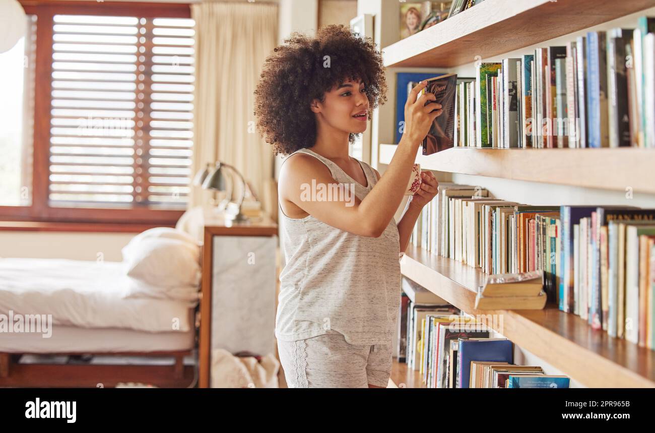 Keine feierlichen Stimmungen. Eine attraktive junge Frau, die zu Hause in einem Bücherregal stöbern kann. Stockfoto