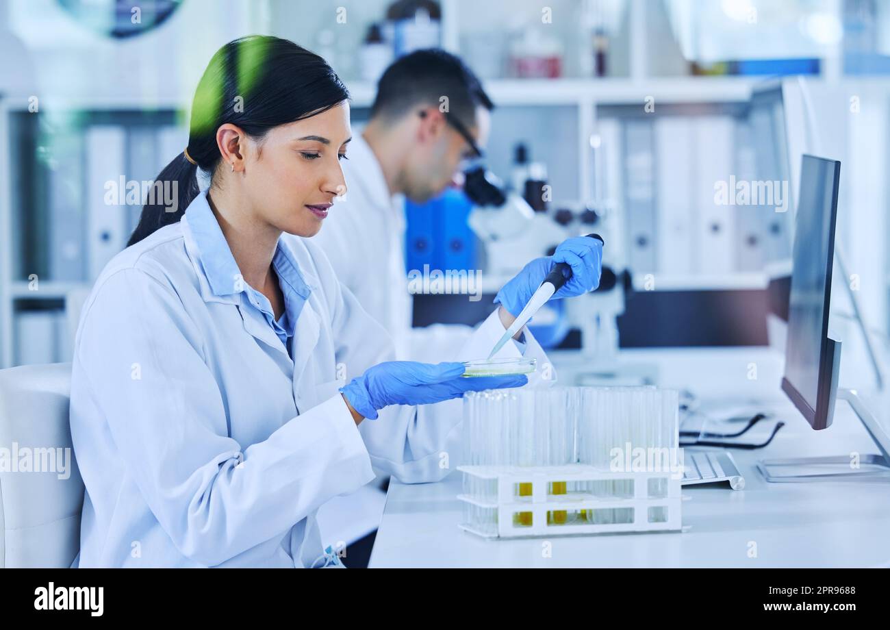 Jede Dosierung sorgfältig vermessen. Eine attraktive junge Wissenschaftlerin, die in ihrem Labor mit einer Kollegin im Hintergrund arbeitet. Stockfoto