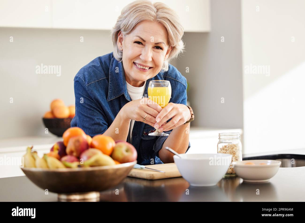 Beginnen Sie den Tag richtig. Eine ältere Frau trinkt zu Hause ein Glas Orangensaft. Stockfoto