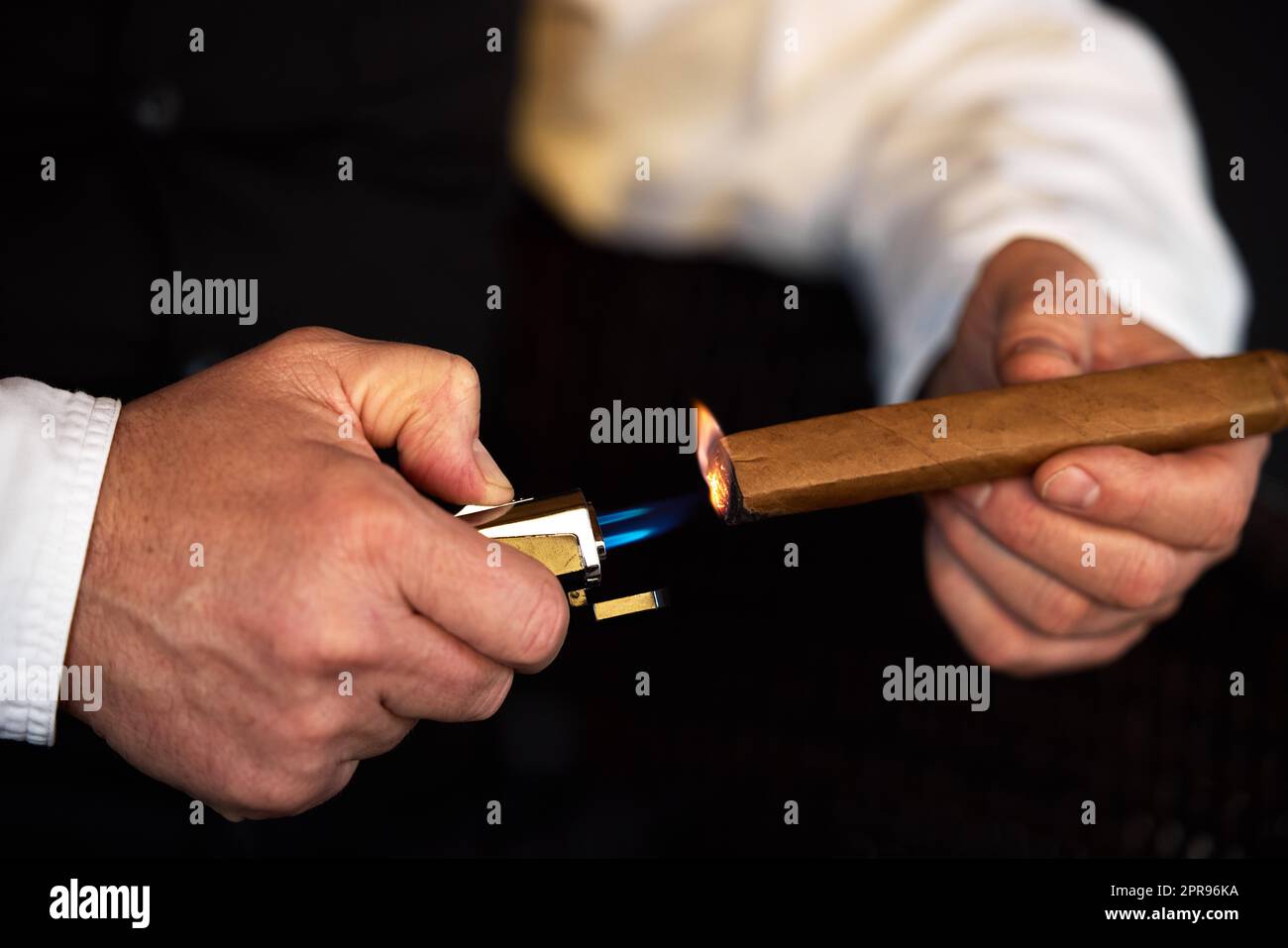 Gönnen Sie sich die feineren Dinge im Leben. Ein unkennbarer Mann zünden eine Zigarre mit einem Feuerzeug an. Stockfoto