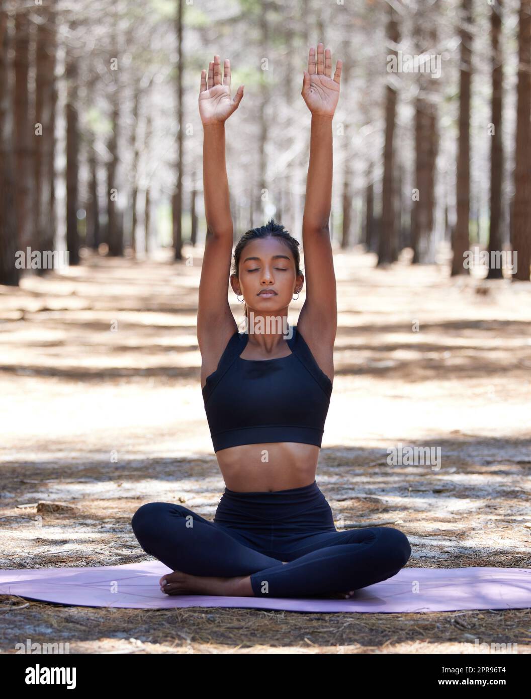 Sammeln guter Energie aus dem Universum. Eine attraktive junge Frau, die allein auf einer Yogamatte im Freien sitzt und meditiert. Stockfoto