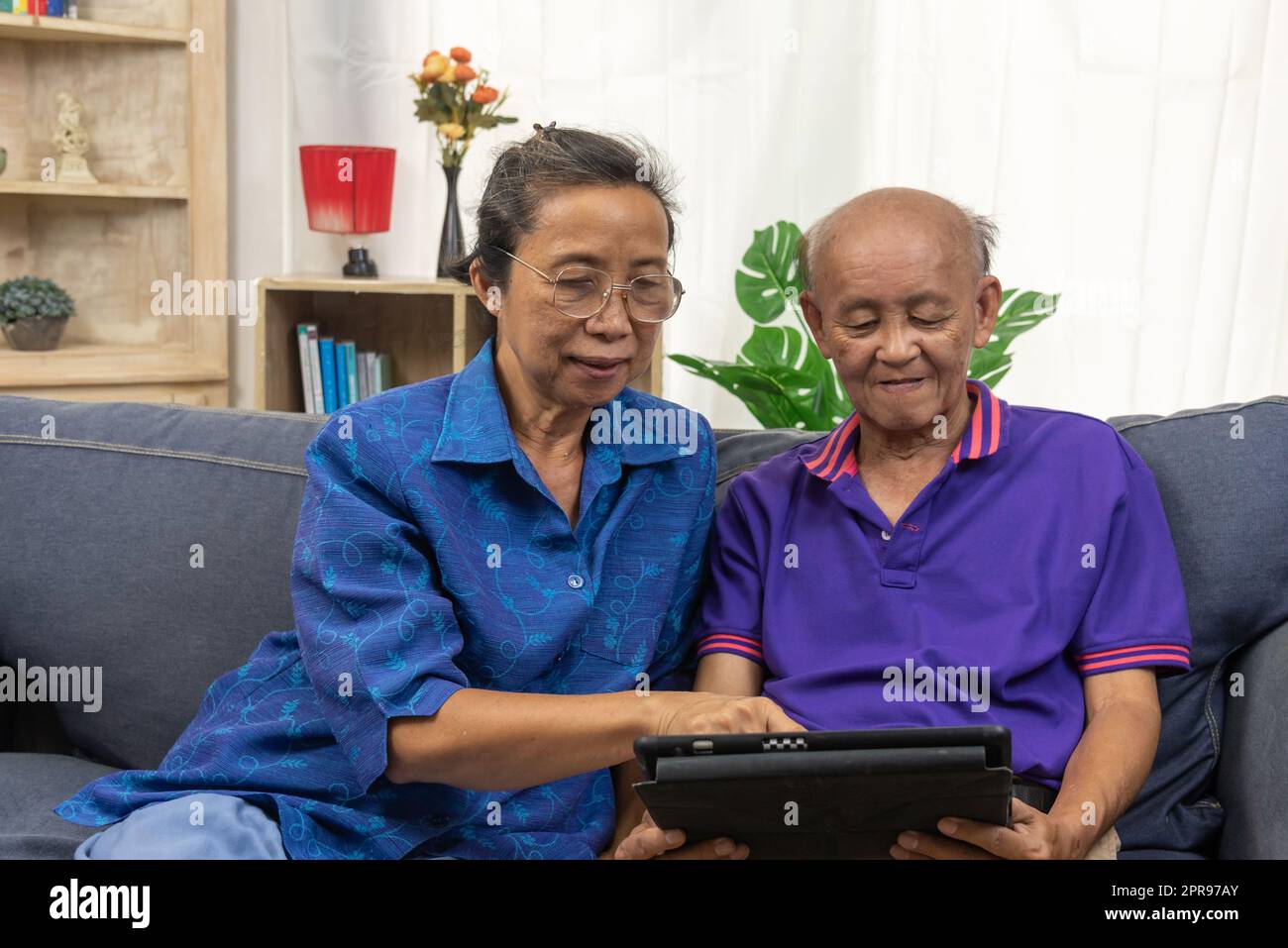 Asiatischer Senior, der zu Hause Tablet-Technologie für die Internetkommunikation auf dem Sofa verwendet. Stockfoto