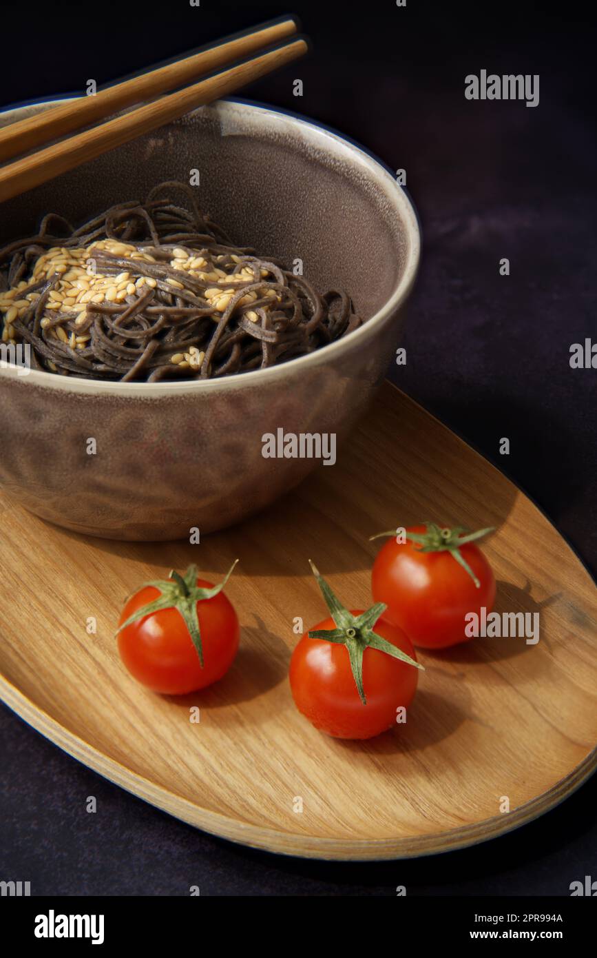 Exquisites Gericht mit schwarzen Nudeln mit einem Hauch von Eleganz. Die Nahaufnahme einer leuchtend roten Kirschtomate ist perfekt auf den Hintergrund der Delikatessen abgestimmt Stockfoto