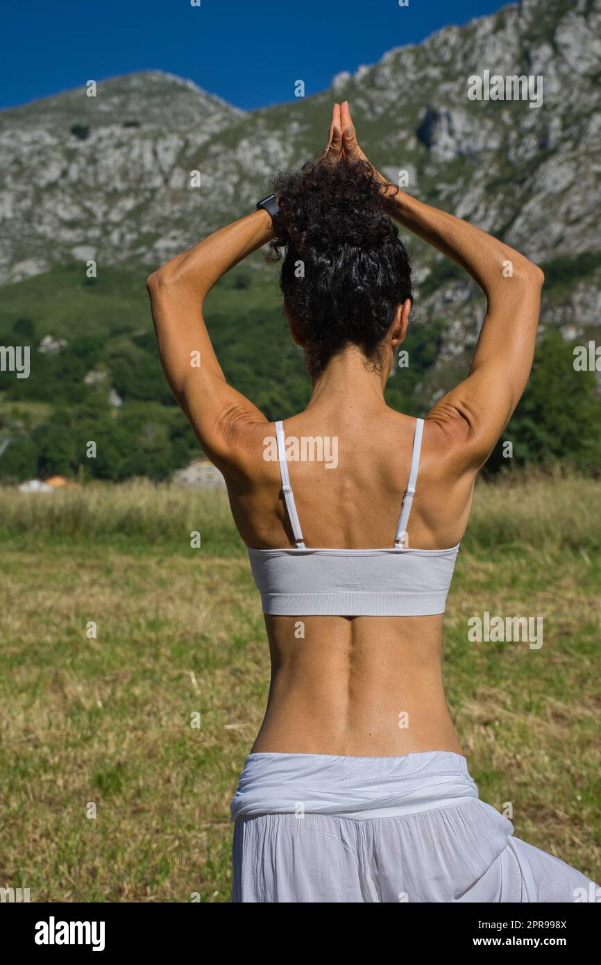 Frau, die Yoga in der Natur auf verschwommenem Hintergrund praktiziert. Weißes Kleid Stockfoto