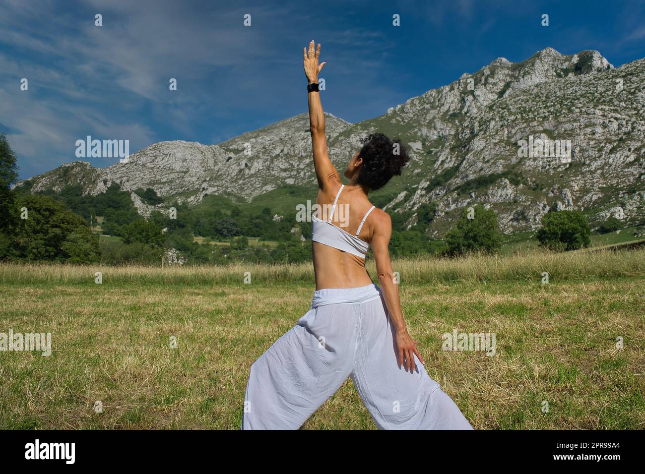 Frau, die Yoga in den Bergen auf unscharfem Hintergrund praktiziert. Weißes Kleid. Stockfoto