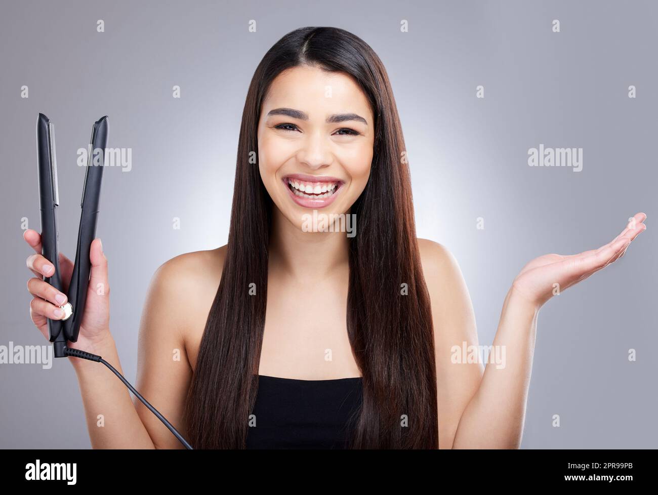 Es ist wirklich ein Wundermittel für Frauen. Studioporträt einer attraktiven jungen Frau, die ihr Haar mit einem flachen Eisen vor einem grauen Hintergrund richtet. Stockfoto