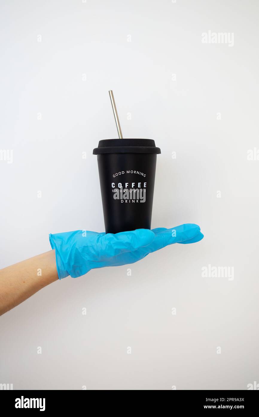 Das Mädchen hält in der Hand ein Metallglas mit Kaffee. Selbstisolierung, Kaffee-Lieferung an die Tür. Kontaktlose Lieferung. Stockfoto