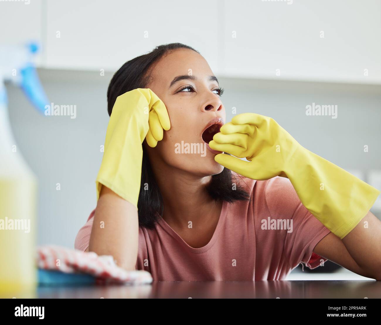 Ich muss ein Nickerchen machen. Eine junge Frau, die eine Pause macht und ihre Küche putzt, um zu gähnen. Stockfoto