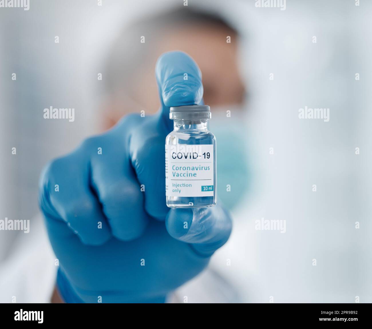 Die Heilung. Nahaufnahme einer Flasche Covid-19-Impfstoff, die von einem nicht erkennbaren männlichen Arzt gegen den Bildschirm gehalten wird. Stockfoto