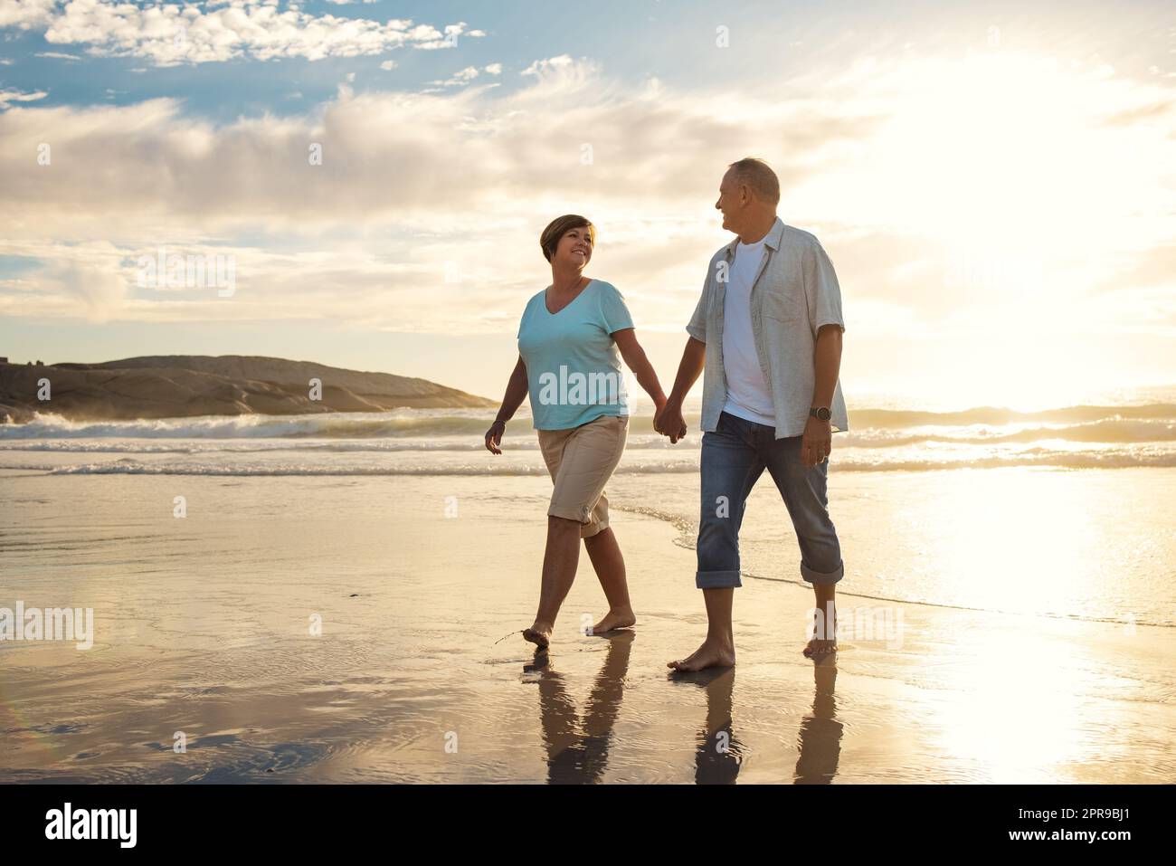 Wir sollten uns mehr Zeit für Spaziergänge am Strand nehmen. Ein reifes Paar hält sich die Hände, während wir am Strand spazieren. Stockfoto