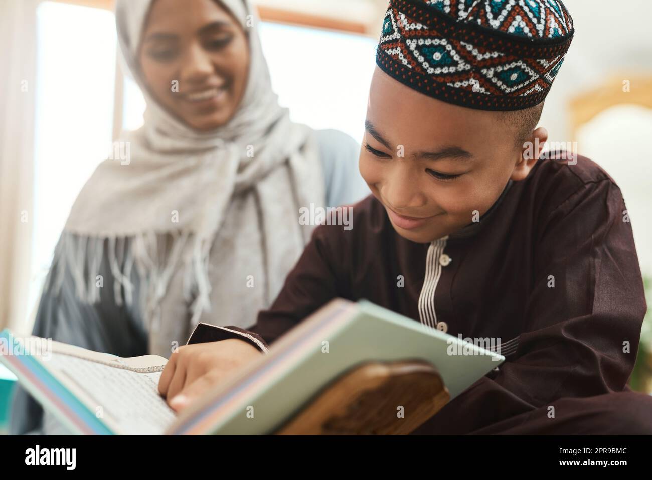 Bildung ist das Anzünden eines Feuers. Eine junge muslimische Mutter und ihr Sohn lesen zu Hause in der Lounge. Stockfoto