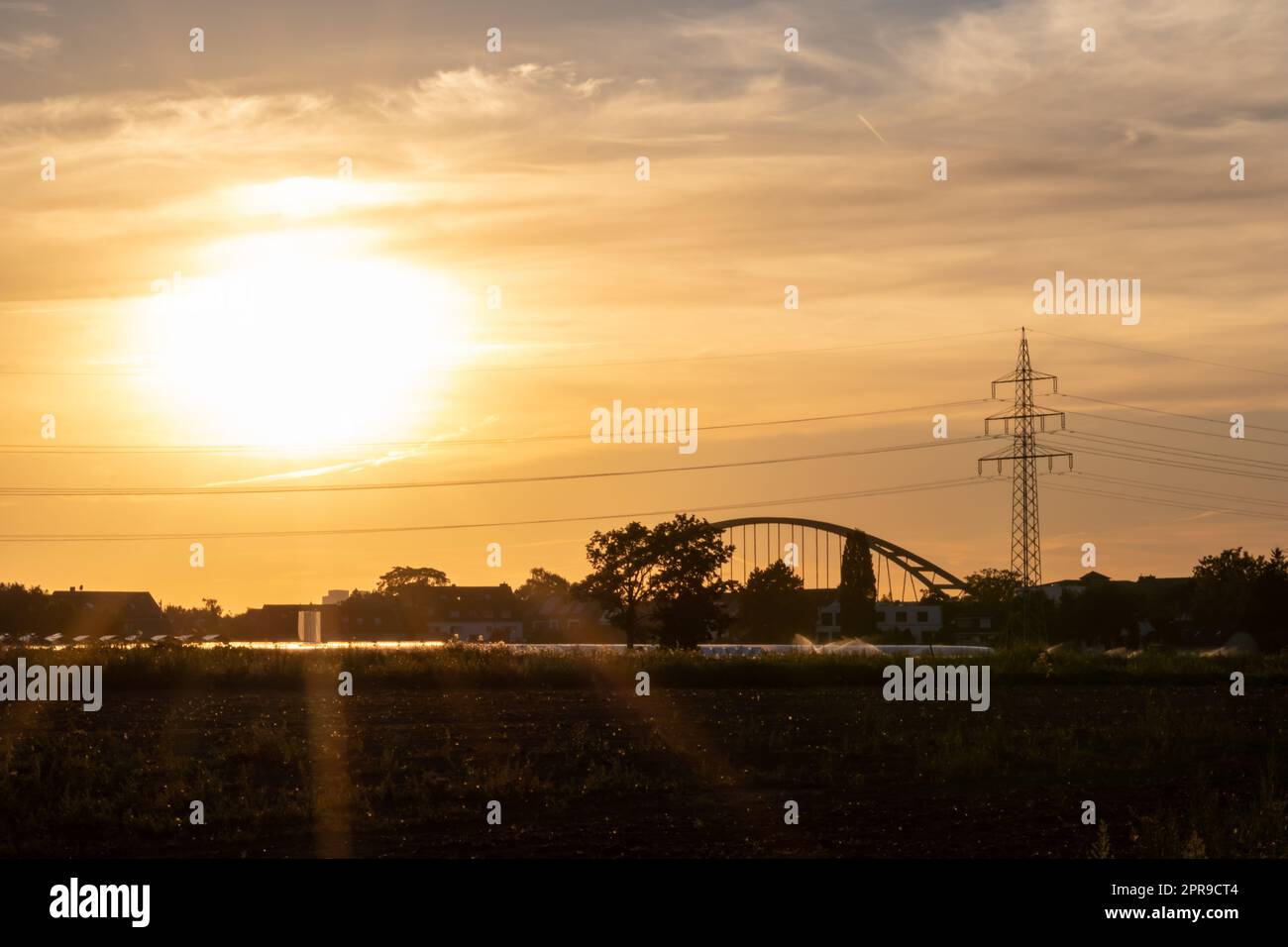 Goldener Sonnenuntergang über Gewächshaussilhouetten mit Brücke und Stromturm für Solarenergie in landwirtschaftlichen Betrieben auf idyllischen Landschaften und ländlicher Landschaft zeigt Glas Gewächshäuser gesundes Gemüse Stockfoto