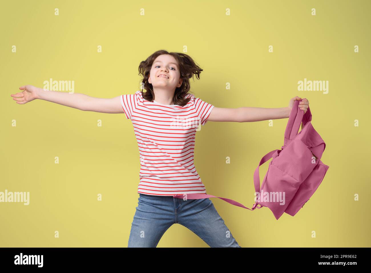 Glückliches Schulmädchen lächelt und springt mit rosa Rucksack, Blick auf die Kamera, auf gelbem Hintergrund Stockfoto